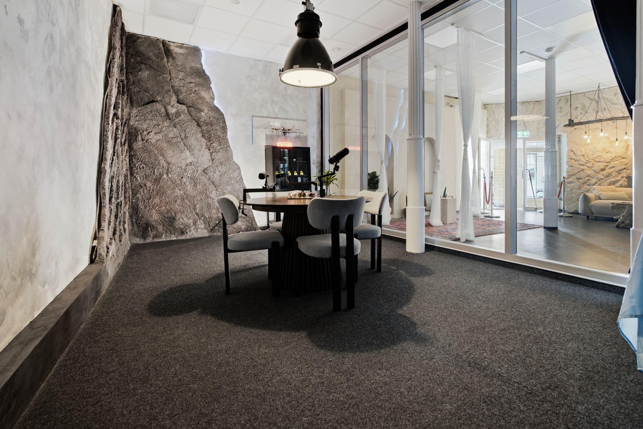 Podcast Room mit rundem Tisch und markanter Steinwand hinter der Glaswand