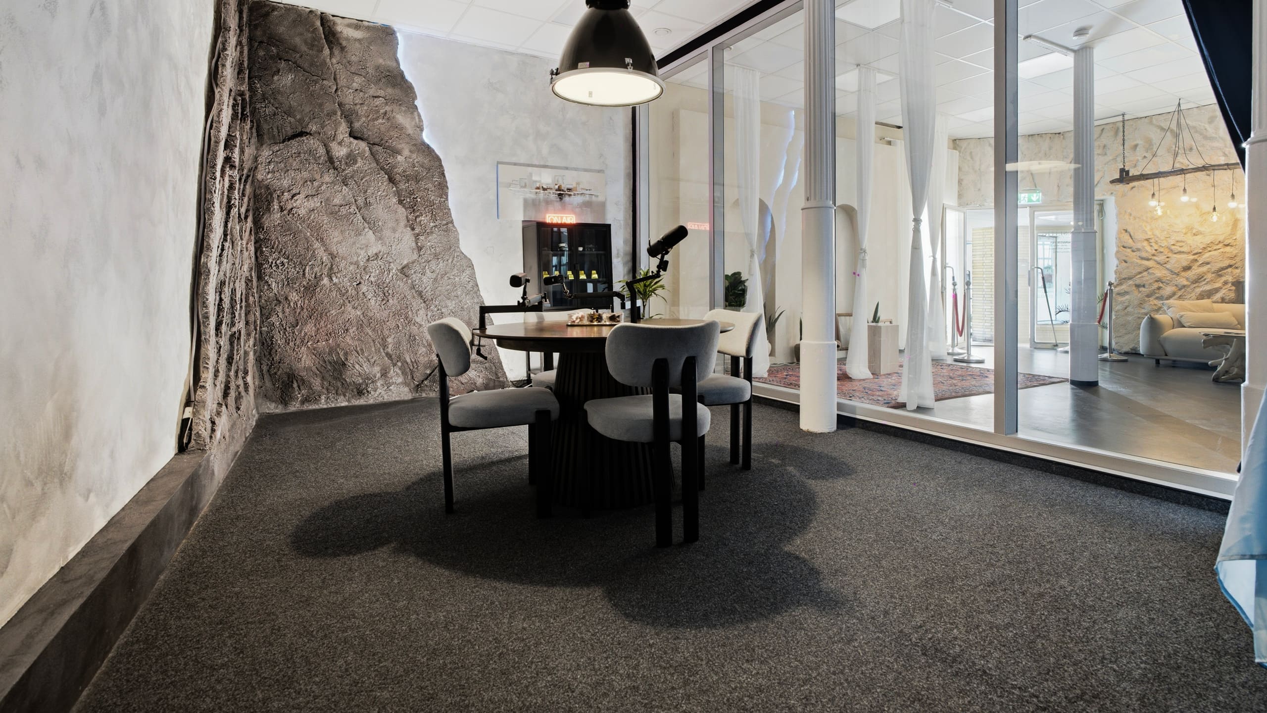 Podcast Room mit rundem Tisch und markanter Steinwand hinter der Glaswand